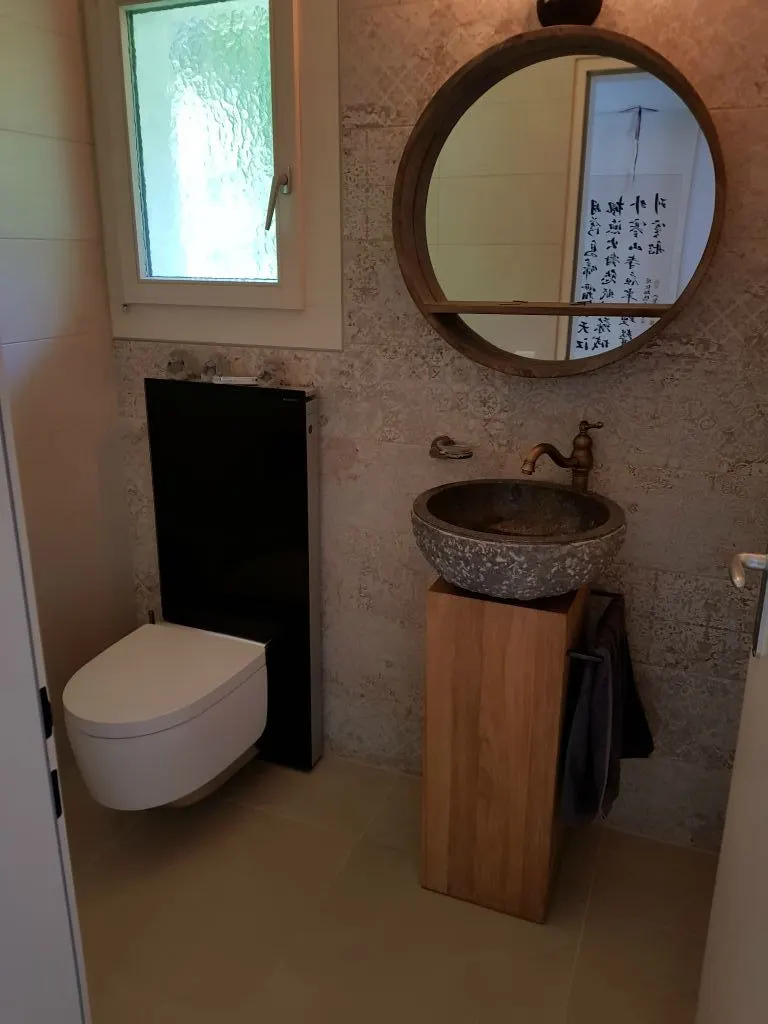 WC mit Naturstein-Waschbecken und rundem Spiegel
